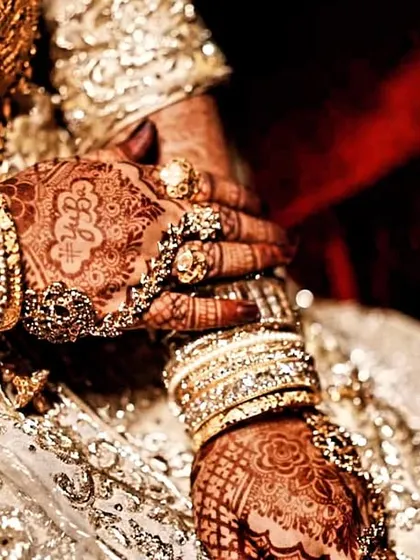 A close-up of a bride's hands, adorned with intricate henna and beautiful jewelry. The stain is deep and rich.