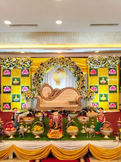 A traditional baby shower (Sreemantham) setup with a yellow marigold backdrop, lotus motifs, and offerings.