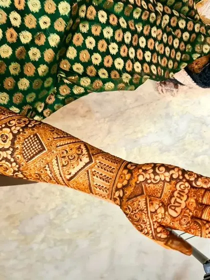 A bridal session in progress, showing the fresh henna paste with the groom's name, 'ATHIQ', artfully hidden in the palm.