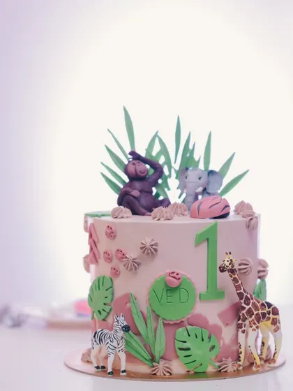 The adorable "Wild One" birthday cake, decorated with fondant jungle animals like a giraffe, zebra, and elephant, and topped with sugar leaves.