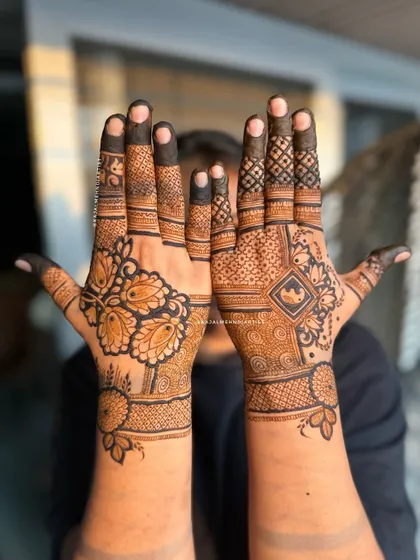 A unique designer henna with contrasting styles on each hand. One palm has a bold, modern floral pattern, while the other features a more traditional grid and motif design.