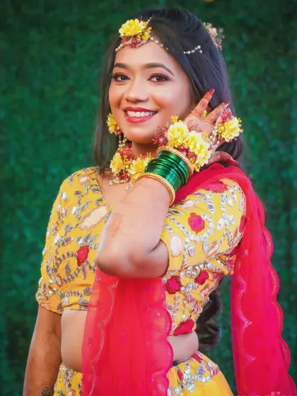 A happy bride showing off her floral hand jewellery during a pre-wedding ceremony like Haldi or Mehendi.