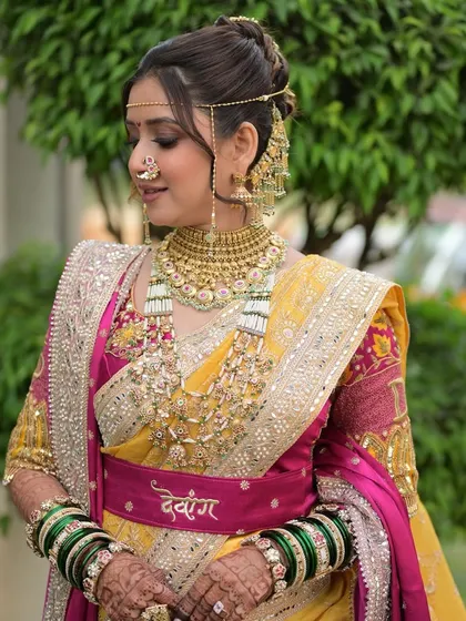 A soft and authentic look for this Maharashtrian bride. The makeup is designed to blend perfectly with the elegance of her traditional style, featuring a custom belt with her husband's name, 'Devang'.