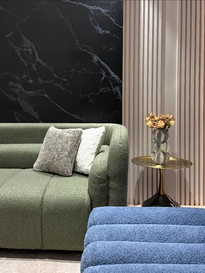This image highlights the material palette of the living room, with a green boucle sofa, a blue textured bench, and a black marble accent wall, all tied together with a brass side table.