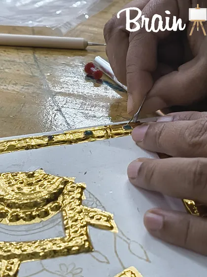 A close up of hands using a tool to perfect the edges of gold foil work, demonstrating the precision taught in our classes.