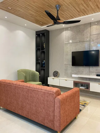The living room features a comfortable rust-colored sofa and a sleek TV unit set against a textured stone-like wall panel, creating a modern yet warm and inviting space.