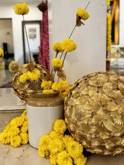 An artistic arrangement of marigolds in a traditional ceramic pot, paired with golden gota patti spheres, blending earthy textures with festive shimmer.