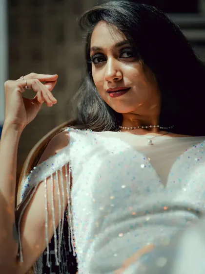 A sun-kissed, artistic shot highlighting the sparkle of the white sequin gown and the delicate pearl necklace.