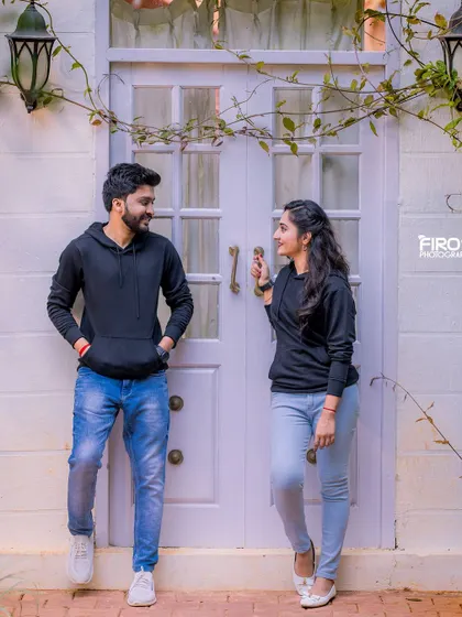 A cool, casual pose in front of a white door. The couple's matching black hoodies and their relaxed stances create a modern and stylish look.