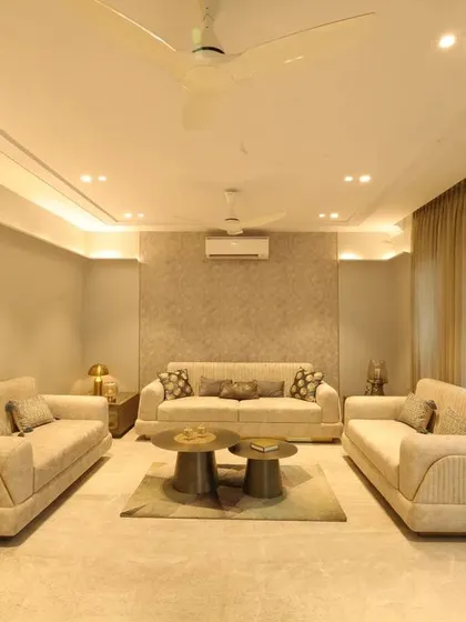 The "Monochrome Oasis" drawing room in Noida showcases a sophisticated palette of beige and grey, with a textured wallpaper accent wall and plush cream sofas.