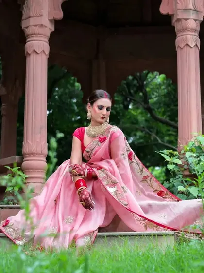 A regal, seated pose within the stone gazebo. The model's posture is elegant, and the pink saree drapes beautifully over the steps.