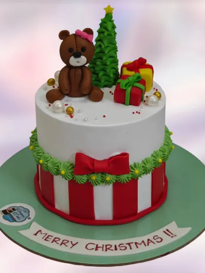 A festive Merry Christmas cake with a teddy bear, a Christmas tree, and presents. A sweet centerpiece for a holiday celebration.