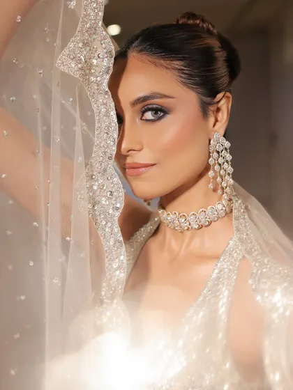 An artistic shot through the sheer, sparkling cape. This highlights the dramatic eye makeup and the flawless skin, creating a sense of mystery and elegance.