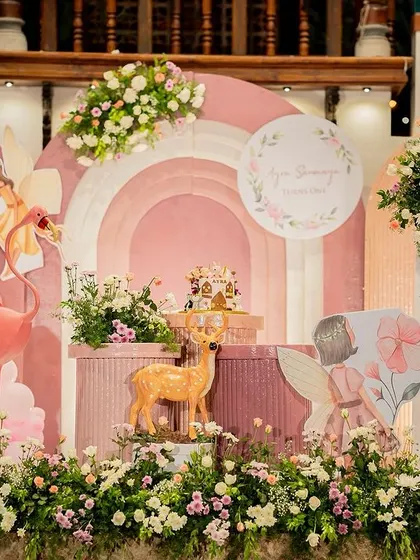A whimsical woodland fairy theme in soft pastel pinks. This setup features arched backdrops, balloon garlands, and adorable deer and fairy cutouts for a magical first birthday.