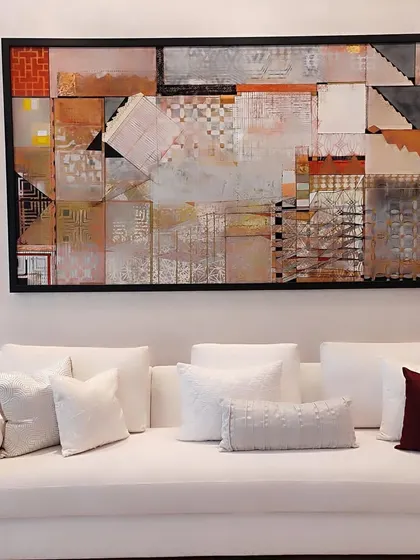 A stunning piece of framed abstract art, featuring a collage of geometric patterns and textures, hangs above a minimalist white sofa. This showcases how our art panels can serve as the focal point of a room.