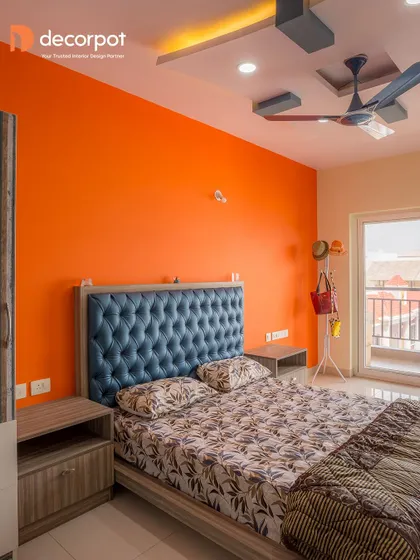 A vibrant bedroom with a bold orange accent wall that makes the tufted blue headboard pop. This design proves that a strong color choice can create a joyful and energetic personal space.