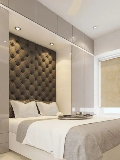 This compact bedroom features a beautiful tufted headboard set into a niche, surrounded by glossy, handle-less wardrobes. The design is a perfect example of maximizing storage in a small space.