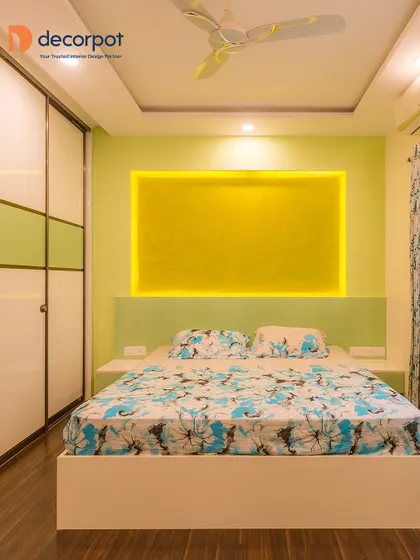 A bright and cheerful bedroom with a lime green and yellow color scheme. The backlit textured panel behind the bed serves as a unique headboard and a source of ambient light.