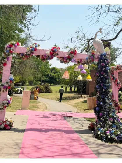 A unique and grand entrance piece. A white peacock with a magnificent tail made of blue and purple flowers stands beside a pink floral arch, creating a truly memorable statement.