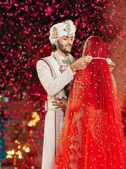 A shower of red rose petals rains down on the couple as they exchange garlands.