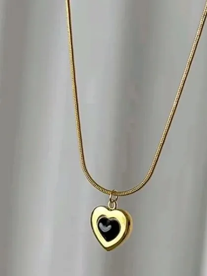 This necklace features a unique double-heart pendant with a black inner heart, set on a gold-toned snake chain. It's a stylish and modern take on a classic design.
