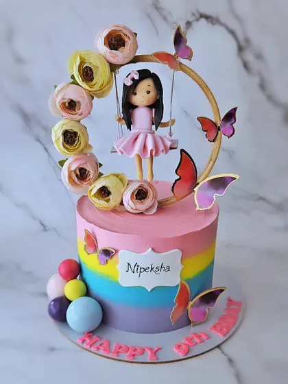A swing cake for Nipeksha's 9th birthday. This butterscotch cake with a rainbow base features a hand-sculpted girl on a floral swing, surrounded by butterflies.