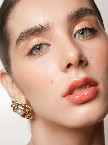 An extreme close-up showing the details of the skin work. You can see the glossy finish on the lips and the subtle, peachy tones on the eyes.