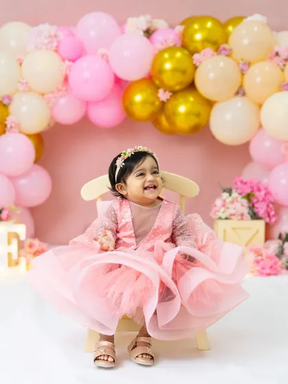 Pretty in pink for her first birthday! This little princess is all smiles in her beautiful ruffled dress, surrounded by a lovely arch of pink, white, and gold balloons.
