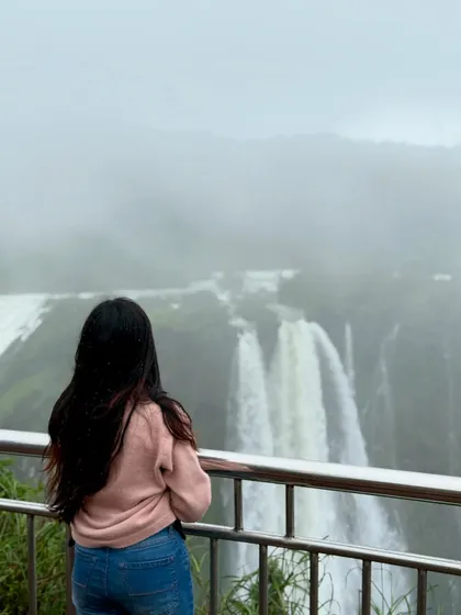 A trekker gazes at the majestic Jog Falls, shrouded in mist during the monsoon. It's a truly beautiful and humbling sight.