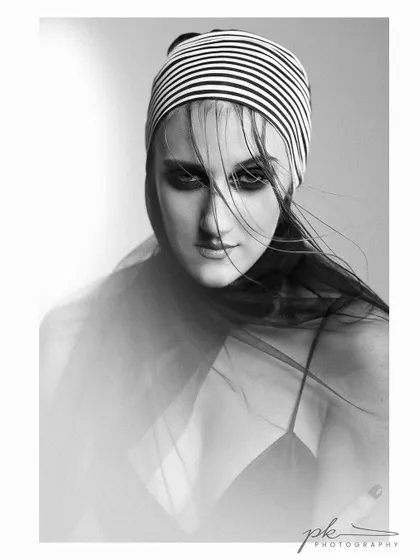 An artistic black and white portrait with a slow shutter effect, creating a sense of movement and mystery. The striped headscarf adds a bold graphic element.