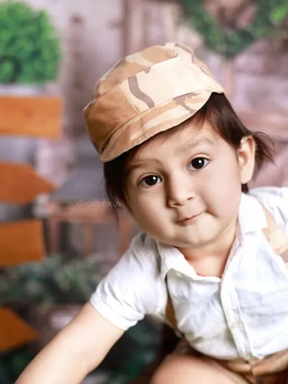 A charming close-up of a little boy in a camo cap, peeking at the camera. The outdoor setting allows for beautiful, naturally lit portraits.