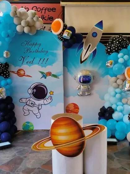 An outer space adventure theme for a 6th birthday. This decoration features astronaut and rocket cutouts, planet props, and a balloon arch in shades of blue and black, creating a galaxy-themed party perfect for a young explorer.