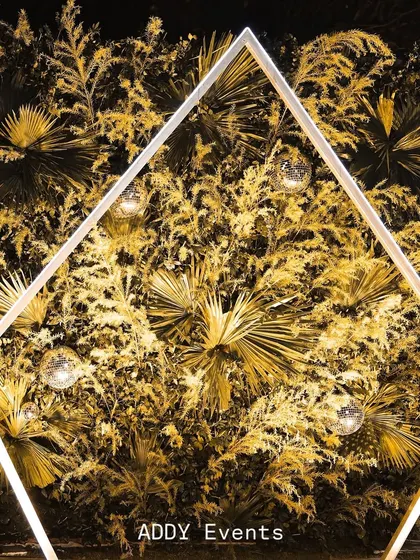 This geometric selfie point, framed with an illuminated diamond shape and backed by a lush wall of golden-lit foliage and disco balls, is designed to be an irresistible photo opportunity for guests.