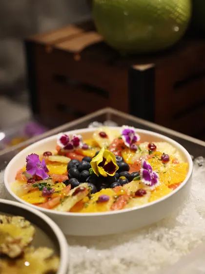 A beautiful fruit salad with citrus segments, blueberries, and edible flowers. The presentation is as delightful as the taste, adding a touch of natural beauty to the buffet line.
