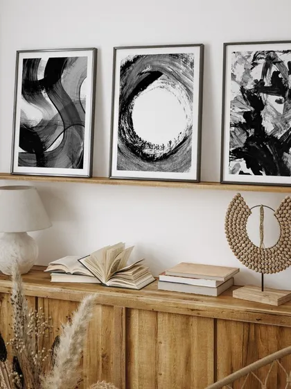 This set of three abstract black brushstroke prints offers a powerful and expressive statement. Displayed on a shelf, they add a touch of modern, artistic sophistication to the room.