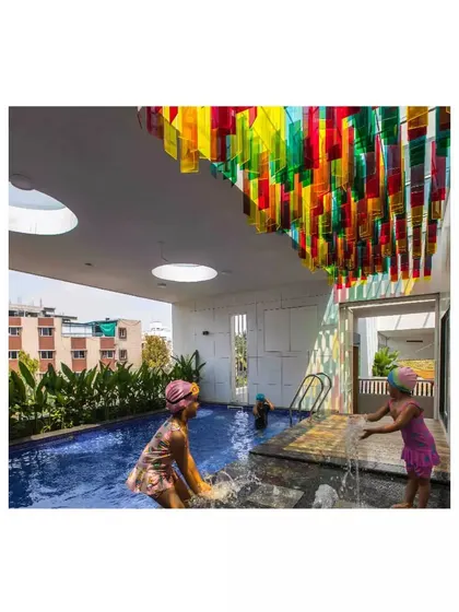 The rooftop swimming pool at the 'Toy Story' preschool is sheltered by a colorful canopy of translucent panels. This feature casts a playful, rainbow-colored light onto the water, making swim time a magical experience for the children.