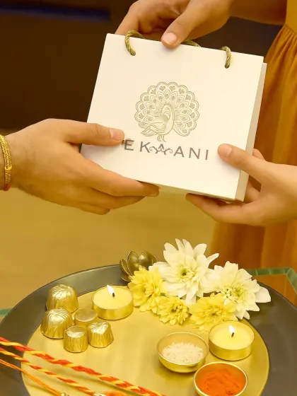 A moment of exchange during Rakhi, where a gift in my signature peacock-branded bag is given. The accompanying thali with diyas and sweets completes the scene of festive love and tradition.