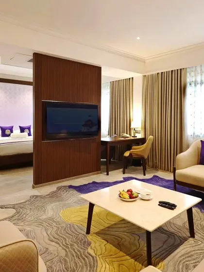 A spacious suite at Vivanta Bengaluru, with a partition separating the living and sleeping areas. The design uses a vibrant rug and purple accents to create a lively yet sophisticated atmosphere.