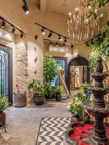 The view from the entrance captures the key elements of our design: the central water feature, lush indoor plants, and racks of vibrant designer clothing. The black and white chevron floor tiles add a graphic, modern contrast to the vintage decor.