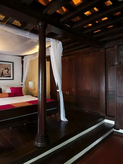 The interior of a restored heritage cottage at the Niraamaya Resort. We preserved the original dark wood structure, including the intricate ceiling and a traditional four-poster bed, to offer an authentic and luxurious experience of Keralan living.