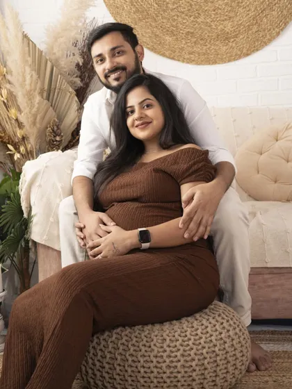 A cozy and warm maternity portrait. The earthy tones of the outfits and the boho-chic studio setup create a comfortable and loving atmosphere.