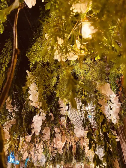 A close-up of the enchanted forest entrance tunnel. The ceiling is a dense mix of green foliage, white flowers, and hanging crystal chandeliers, creating a lush and magical effect.
