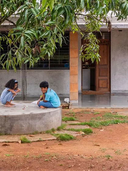 Children playing a game on the concrete plinth at "Aamra." The house is designed to be a backdrop for life's simple moments, fostering engagement with the bucolic surroundings.