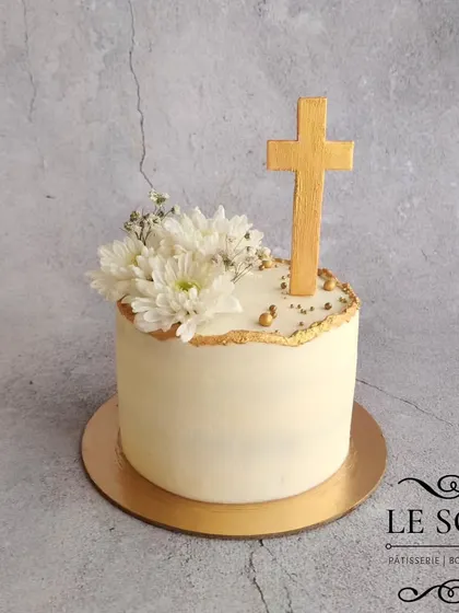 This simple and elegant cake was for a holy communion. The half-kg Ferrero Crunch cake is finished with smooth white buttercream, a gold-dusted cross, and fresh white flowers.