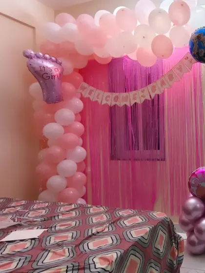 An intimate and cozy welcome home setup for a baby girl. A pink balloon arch and "Welcome Baby" banner transform the bedroom into a sweet, celebratory space for the new mother and child.