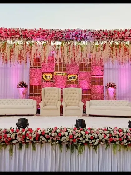 This reception stage is a vision in pink, featuring a ceiling of hanging floral strings and a dense flower border. The combination of plush white seating and warm pink lighting creates a romantic and luxurious atmosphere.