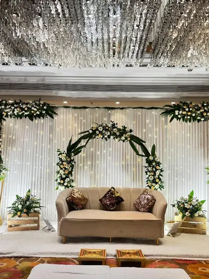 A beautiful rustic-chic stage setup at Jaypee Siddharth. The design features a semi-circular floral arch, white drapes with fairy lights, and wooden crates for a touch of rustic charm.