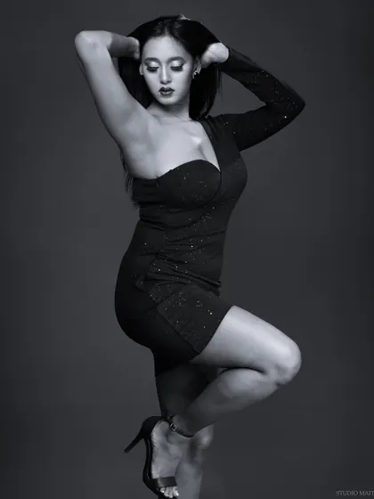 A graceful black and white photo of a model in a one-shoulder black dress. The lighting and pose create an elegant and timeless fashion portrait.