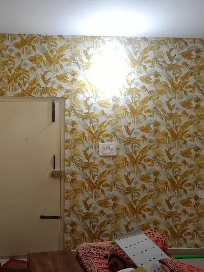 A living room featuring a vibrant tropical leaf wallpaper in shades of yellow and grey. The energetic pattern adds a fun and modern touch to the space.