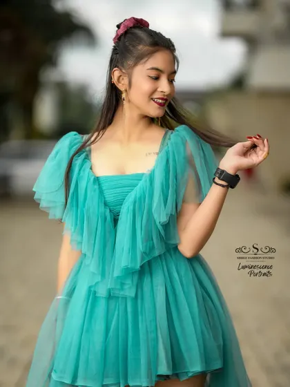 A candid and playful moment, with the model twirling a strand of hair, her teal dress adding a splash of color to the scene.